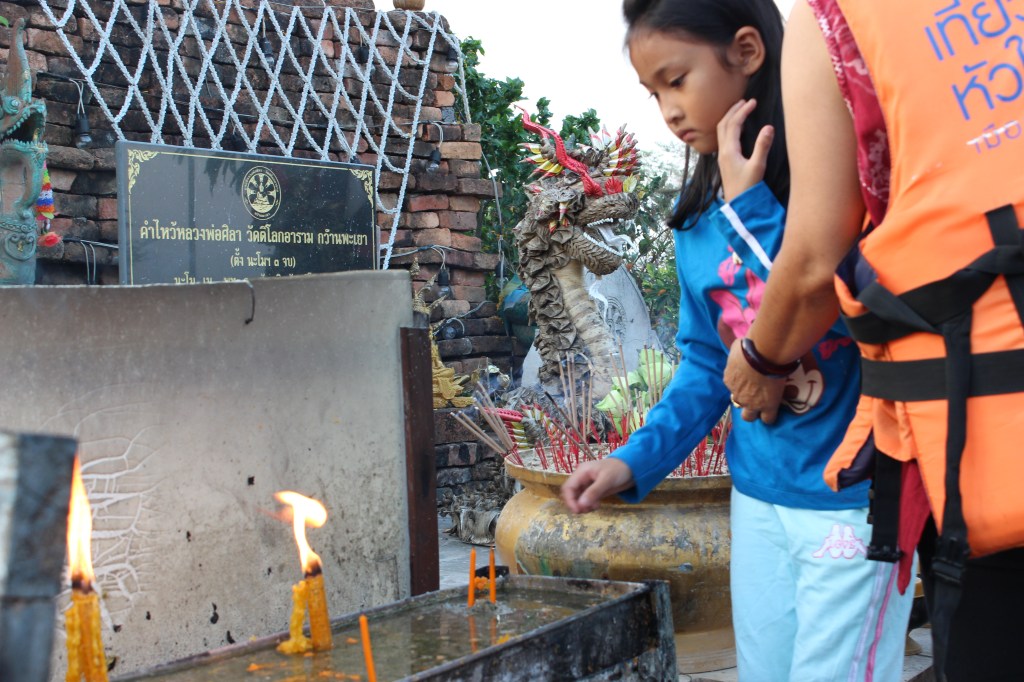 A young girl lighting incense before the Buddha statue.